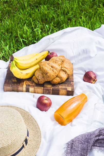 Piquenique de verão na natureza com croissants, suco e frutas em um véu branco entre a grama verde. Lazer na natureza
 - Foto, Imagem