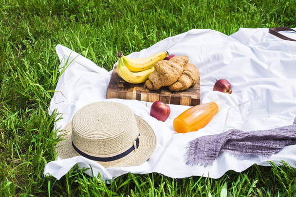Piquenique de verão na natureza com croissants, suco e frutas em um véu branco entre a grama verde. Chapéu de palha de mulher. Lazer na natureza
 - Foto, Imagem