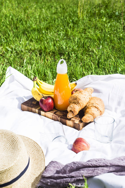 Picnic de verano en la naturaleza con croissants, jugo y fruta sobre un velo blanco entre la hierba verde. Ocio en la naturaleza
 - Foto, Imagen