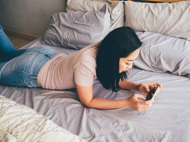 Woman is playing smartphone game on her bed. - Фото, зображення