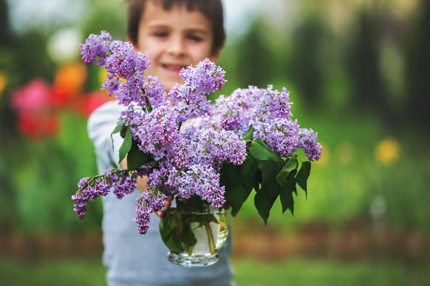 Sweet child, boy, holding vase with lilac flowers in garden, pre - Фото, зображення