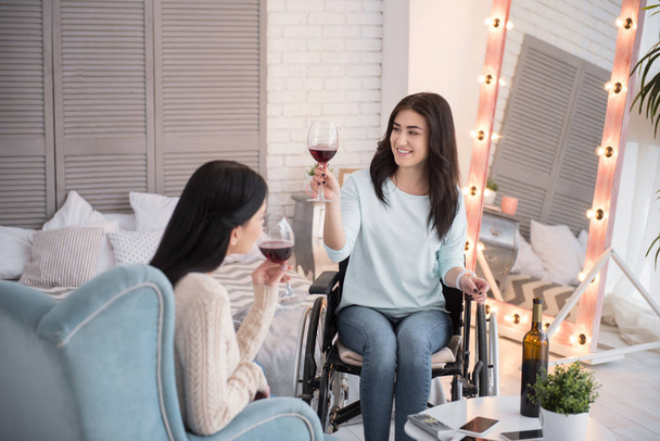 Best friends. Glad handicapped woman tasting wine and talking to friend - Фото, изображение