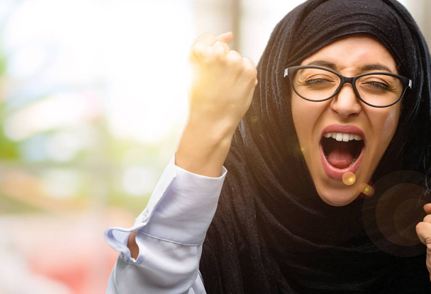 Mujer árabe joven vistiendo hijab feliz y emocionada celebrando la victoria expresando gran éxito, poder, energía y emociones positivas. Celebra el nuevo trabajo alegre
 - Foto, imagen