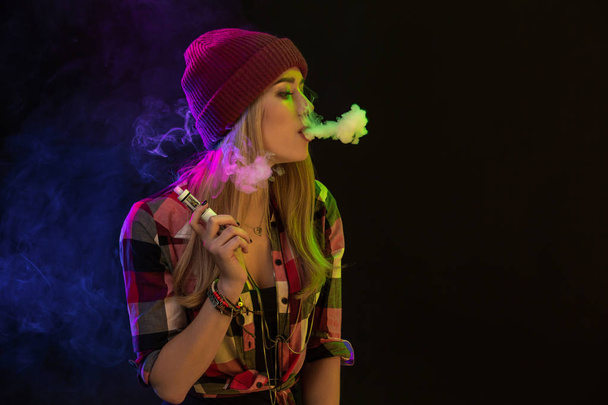 Vaping girl. Young hipster woman vape e-cig on black background. Hip-hop style. Studio shot - Foto, Imagen