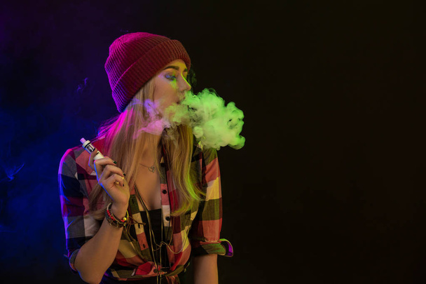 Vaping girl. Young hipster woman vape e-cig on black background. Hip-hop style. Studio shot - Foto, Imagem