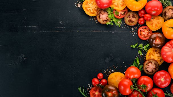 Assortment of colored fresh tomatoes. On a black wooden background. Top view. Copy space. - Foto, Imagen