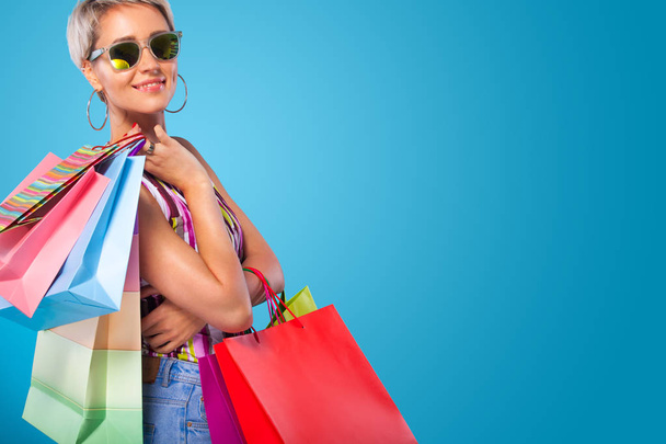 Mujer de compras sosteniendo bolsas de color aisladas sobre fondo azul en vacaciones de viernes negro. Concepto de venta verano
. - Foto, Imagen