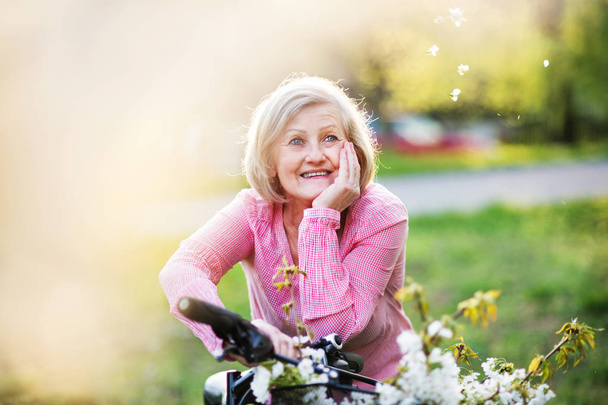 Beautiful senior woman with bicycle outside in spring nature. - Zdjęcie, obraz