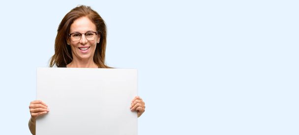 Frau mittleren Alters trägt schwarzes Hemd und Brille mit leerem Werbebanner, gutes Plakat für Werbung, Angebot oder Ankündigung, große Werbetafel isoliert blauen Hintergrund - Foto, Bild