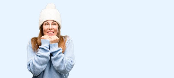 Μέσης ηλικίας γυναίκα που φοράει καπάκι χειμώνα μαλλί τρομοκρατημένος και νευρικό εκφράζοντας άγχους και πανικού χειρονομία, συγκλονισμένοι απομονωμένες μπλε φόντο - Φωτογραφία, εικόνα