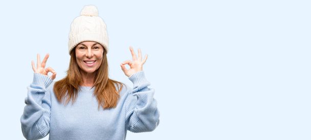 中年の女性両手瞑想とリラクゼーションを表現する [ok] の手話をやってウール冬帽をかぶって分離青色の背景 - 写真・画像