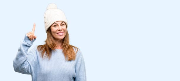 指番号を 1 つの孤立した青色の背景を上げるウール防寒帽を身に着けている中年女性 - 写真・画像