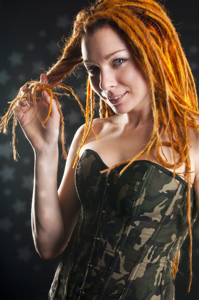 Beautiful girl with red dreadlocks posing in military corset - Photo, image