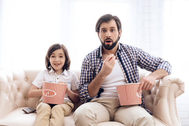 Bearded father with small son is watching thrilling film, eating popcorn. - Zdjęcie, obraz