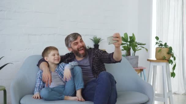 Funny man loving father is taking selfie with his cheerful son, laughing and gesturing, posing for camera. Self-portrait and happy family concept. - Záběry, video