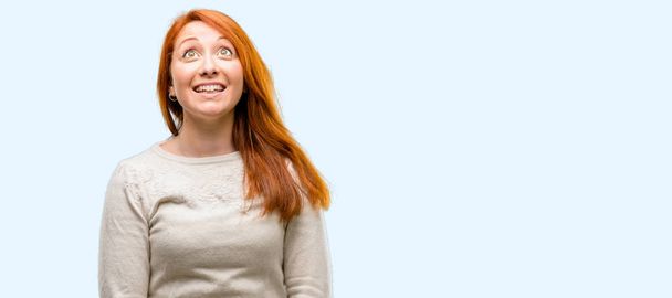 schöne junge rothaarige Frau glücklich und überrascht jubelnd ausdrückende wow Geste isoliert über blauem Hintergrund - Foto, Bild