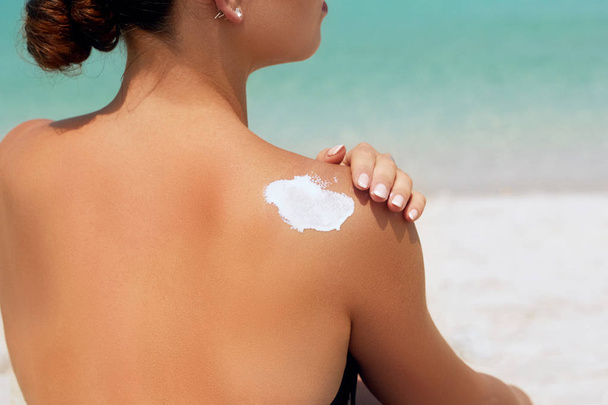 女性は日焼けした肩に日焼け止めクリームを適用します。スキンケア。体太陽保護 suncream。ビキニ帽子女の背中に保湿日焼け止めローションを適用します。. - 写真・画像