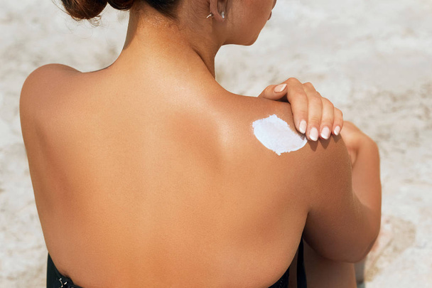attraktive Frau mit gesunder Haut, die Sonnencreme auf die Schulter aufträgt und weißen Sonnenhut trägt - Foto, Bild