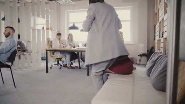 2 つの女性の同僚のドリー ショット オフィス ソファから立ち上がって、近代的なオフィスに徒歩します。ガラス貫通 4 k 表示します。. - 映像、動画