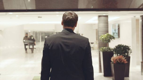 Rear view of businessman near the reception. Stock. There are glass wall offices. Rear view of businessman in hotel - Photo, Image