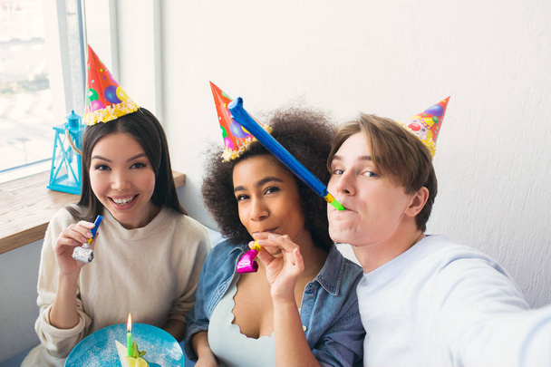 Guy is taking a selfie with his two friends. They are celebrating afro american girls birthday. People wears birthday hats. Also girls have whisltes. - Photo, Image