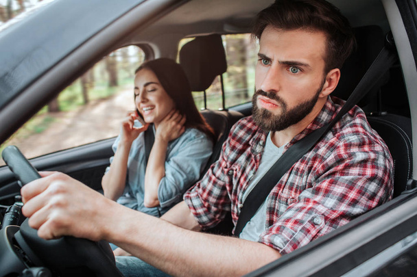 young women is sitting besides man that is driving car. He is upset and unhappy. Guy is looking to the side with serious face - Фото, изображение