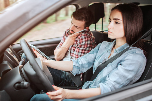 A picture of couple travelling in car. Guy is talking on the phone while girl is driving and paying attention to the road. She looks serious. - Foto, imagen