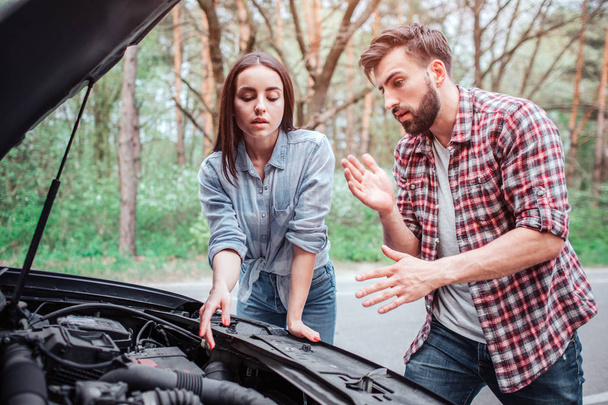 A picture of couple trying to fix the engine of car. It got broken. Girl is pointing to engine while guy is talking to her and getting his hands clean. - Photo, Image