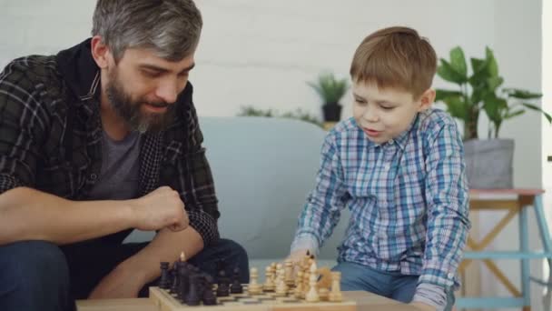 Loving dad is playing chess with his little child, teaching him rules and talking to him. Raising children, intellectual games and happy childhood concept. - Πλάνα, βίντεο