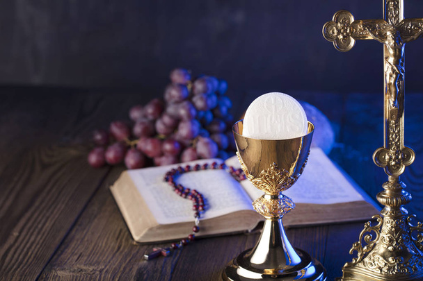 最初の聖体拝領のテーマ。十字架、聖書、ロザリオ、黄金の杯。キリスト教のパンと葡萄のシンボル. - 写真・画像