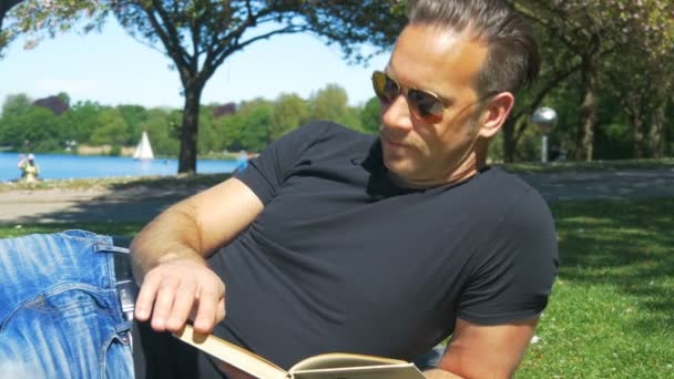 Summer in the city - a man relaxes on the lawn in the park and reads a book - Video