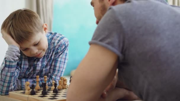 Close-up shot of two people father and son playing chess, thinking about next move and moving chessmen on board. Intellectual hobby and happy family concept. - Imágenes, Vídeo