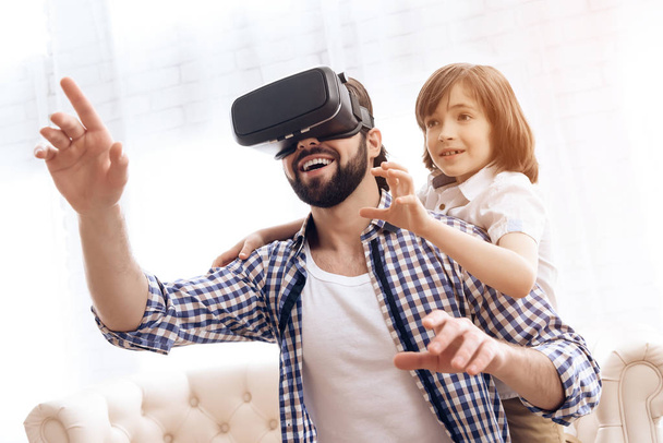 Adult father uses virtual reality glasses together with son at home. - 写真・画像