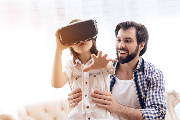 Teenage son uses virtual reality glasses next to father. - Foto, afbeelding
