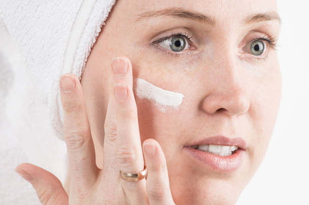 Cosmetics: a girl with a white towel on her head applies a moisturizing cream on her face. - Foto, imagen