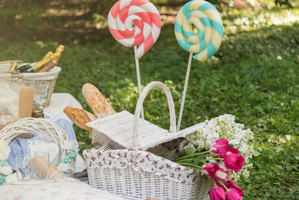 Picnic decorations, cannotier, flowers, fruits. Picnic at the park on the grass: tablecloth, basket, healthy food and accessories, top view, bread, baguette, alcohol, big lollipops. Happy mothers day. - Photo, Image
