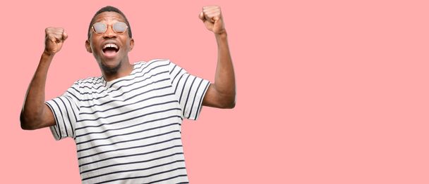 L'uomo nero africano indossa occhiali da sole felici ed eccitati celebrando la vittoria esprimendo grande successo, potenza, energia ed emozioni positive. Celebra il nuovo lavoro gioioso
 - Foto, immagini