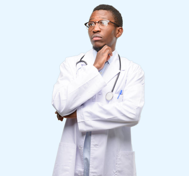 Young black doctor, medical professional thinking and looking up expressing doubt and wonder - 写真・画像