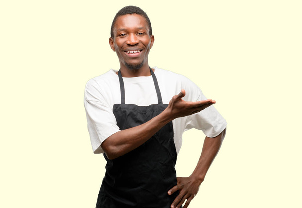 Africano dueño de una tienda con delantal sosteniendo algo en la mano vacía
 - Foto, imagen