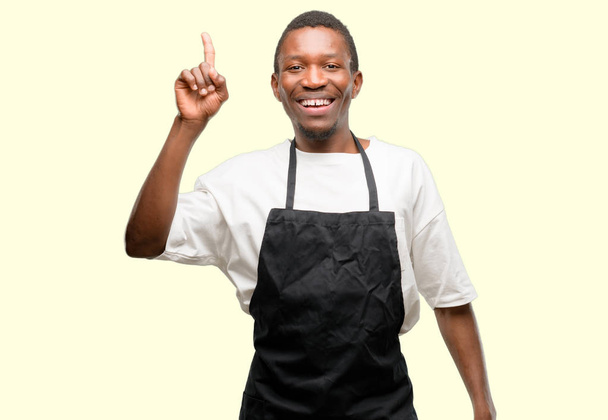 African man shop owner wearing apron pointing away side with finger - Foto, afbeelding