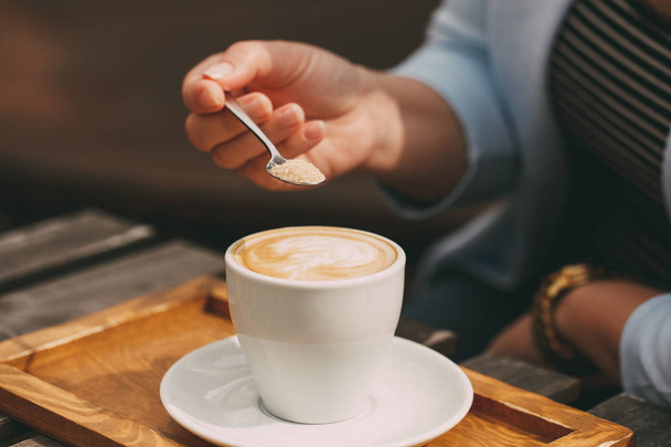 Spoon in a female hand pouring sugar into her coffee cup - Foto, imagen