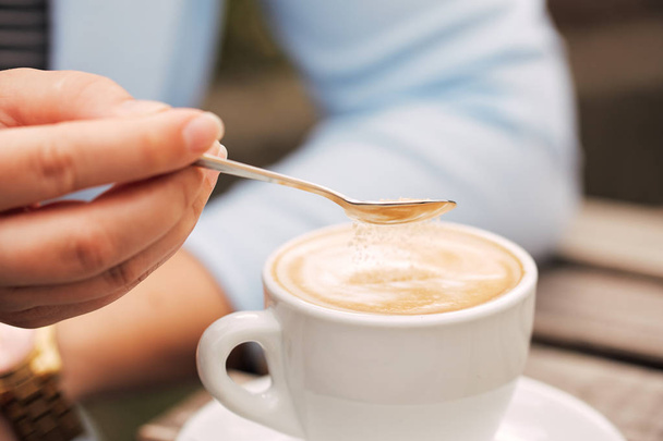 Spoon in a female hand pouring sugar into her coffee cup - Фото, зображення
