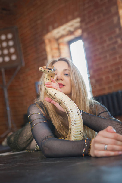 Elegante blonde vrouw liggend op het bed met python - Foto, afbeelding