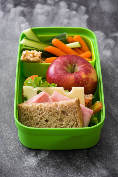 Boîte à lunch scolaire saine : Sandwich, légumes, fruits et jus sur pierre noire
 - Photo, image