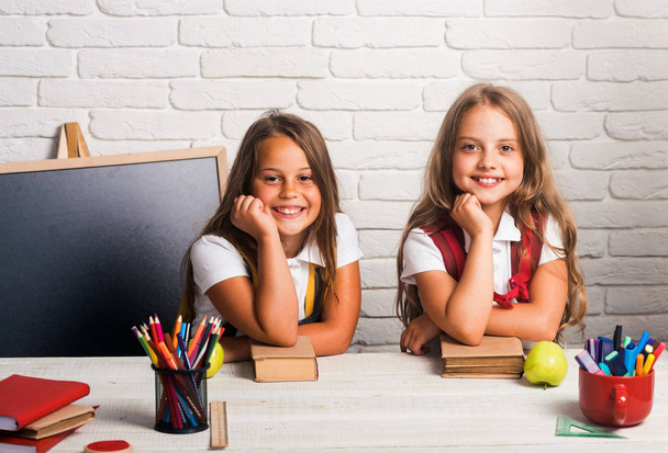 Back to school and home schooling. Happy school kids at lesson in september 1. Little girls eat apple at lunch break. Friendship of small sisters in classroom at knowledge day. School time of girls - Photo, Image