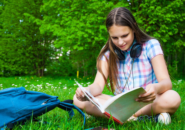 Étudiant étudiant au parc. Joyeuse adolescente heureuse étudiante assise et lisant dehors sur le campus universitaire ou le parc
. - Photo, image