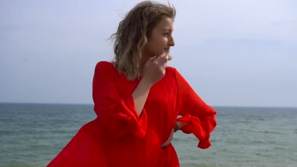 赤いドレスで幸せな若い女は、海岸の崖で楽しい時を過す - 映像、動画