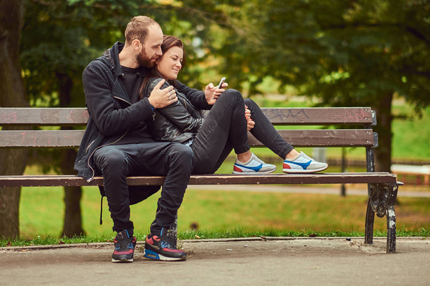 Casal moderno atraente sentado em um banco em um parque
. - Foto, Imagem