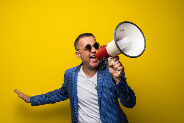 Mature man in sunglasses speaking with loudspeaker isolated on yellow background - Foto, Bild