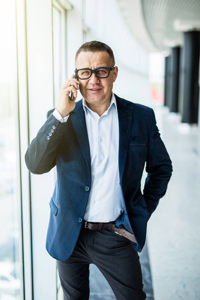 Businessman on the phone. Confident senior man in formalwear talking on the mobile phone and looking at camera in office - 写真・画像